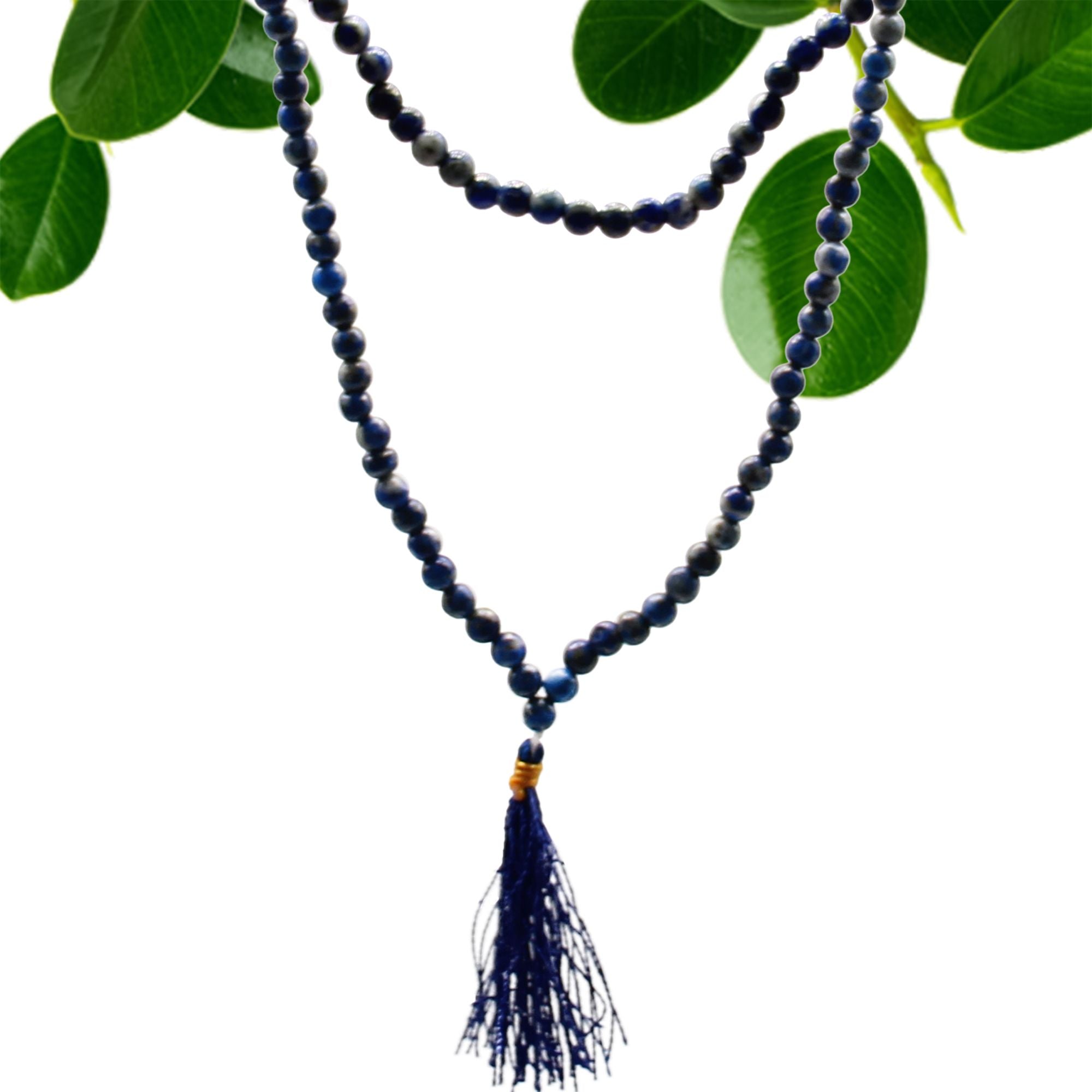 Collier mala 108 perles en pierre naturelle lapis lazuli avec pompon bleu, suspendu avec feuilles vertes en arriere plan, bijou spirituel pour meditation chakra et bien etre