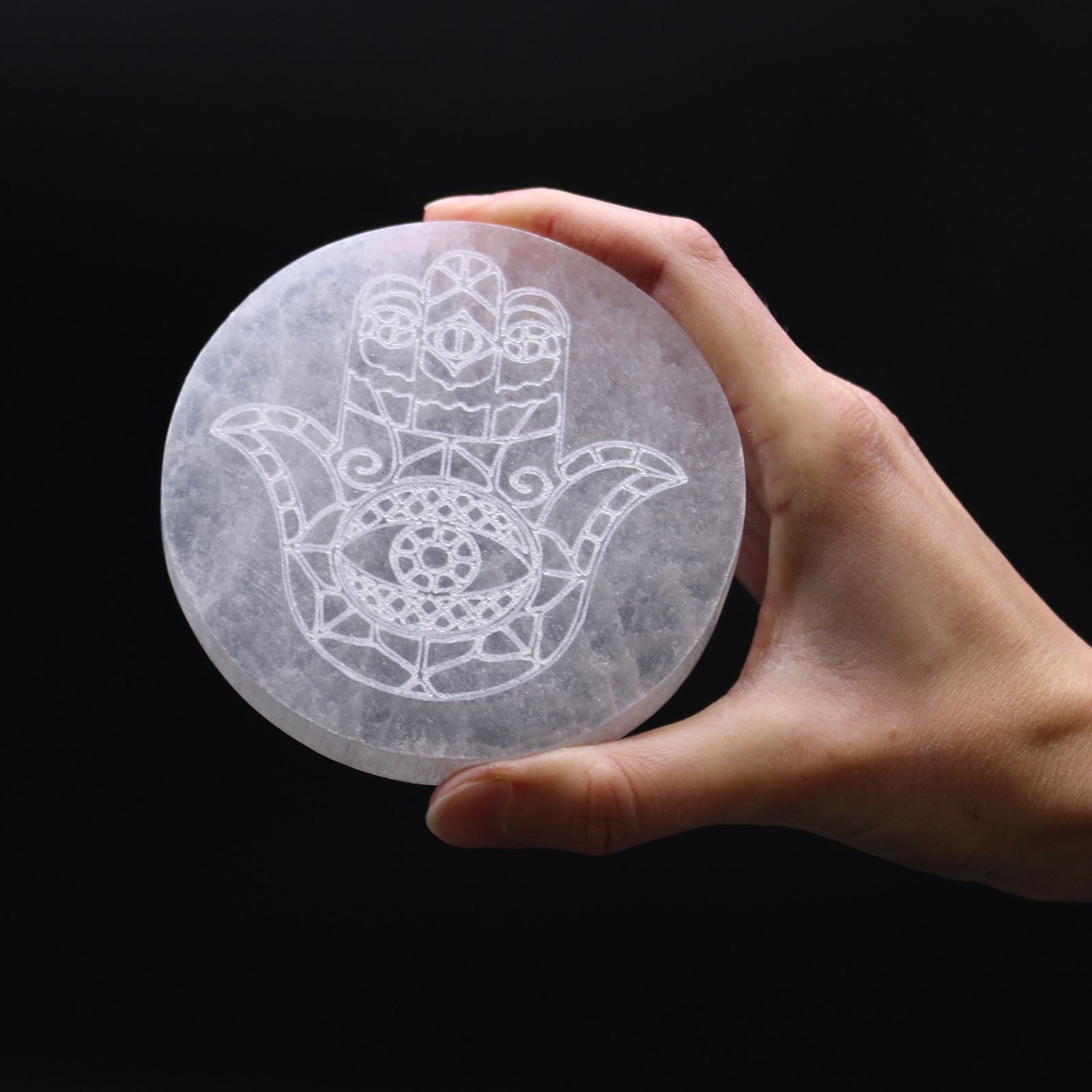 Plaque selenite hamsa tenue en main pour recharger les pierres naturelles et harmoniser les energies