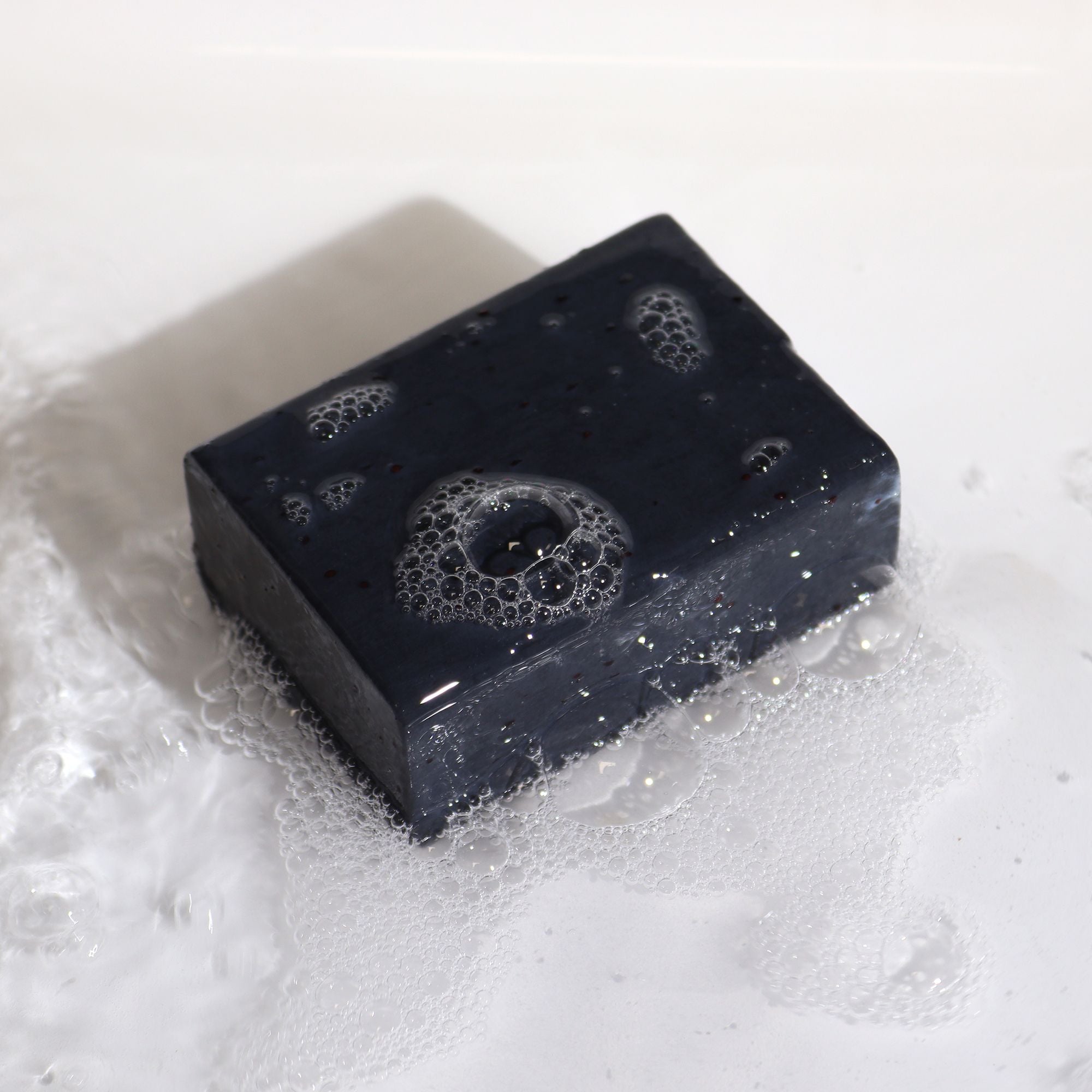 Savon détox charbon actif nettoyage pores peau nette en train de mousser sur table blanche