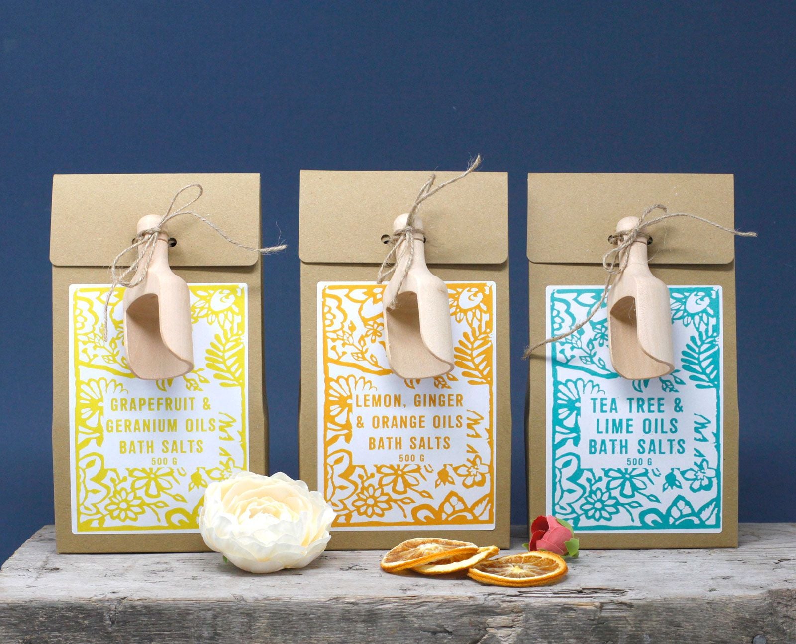 Alignement de sels de bain 500g avec packaging kraft, étiquettes colorées et cuillère en bois dans un décor naturel