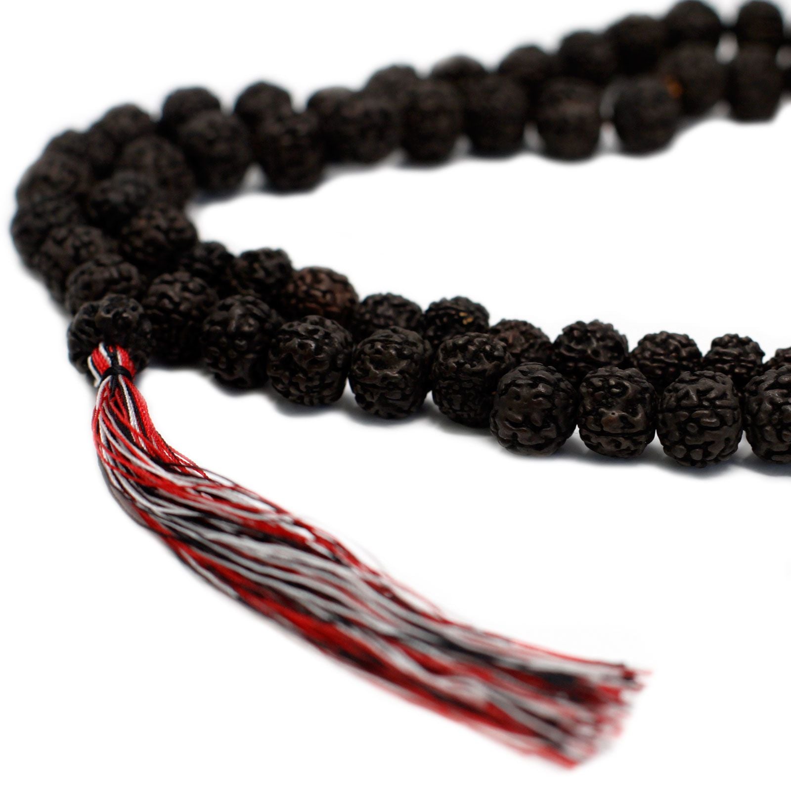 Gros plan sur des perles de rudraksha foncé avec texture détaillée et pompon rouge et blanc attaché au mala.