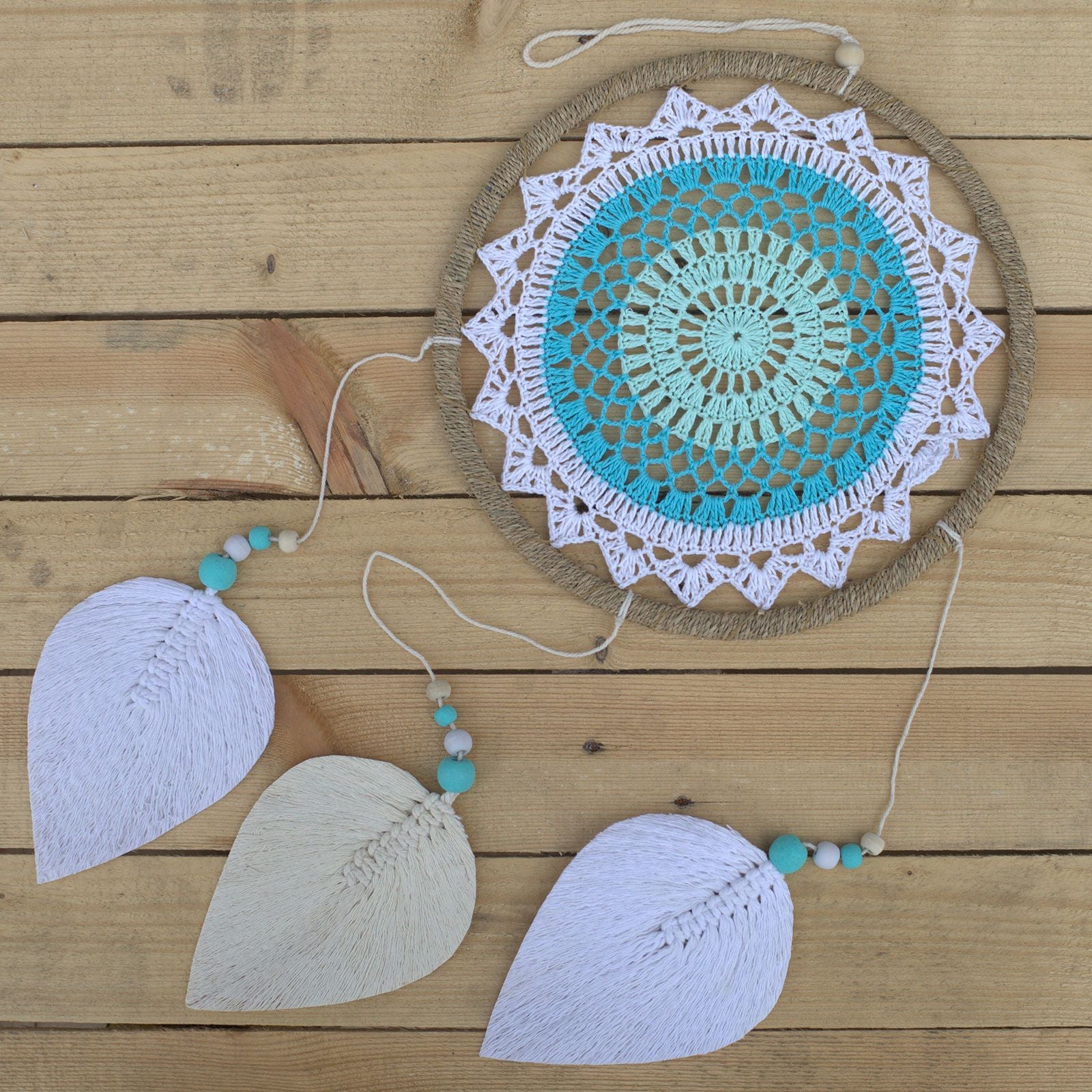 Attrape-rêves turquoise posé sur surface bois avec plumes blanches, idéal pour une décoration bohème apaisante