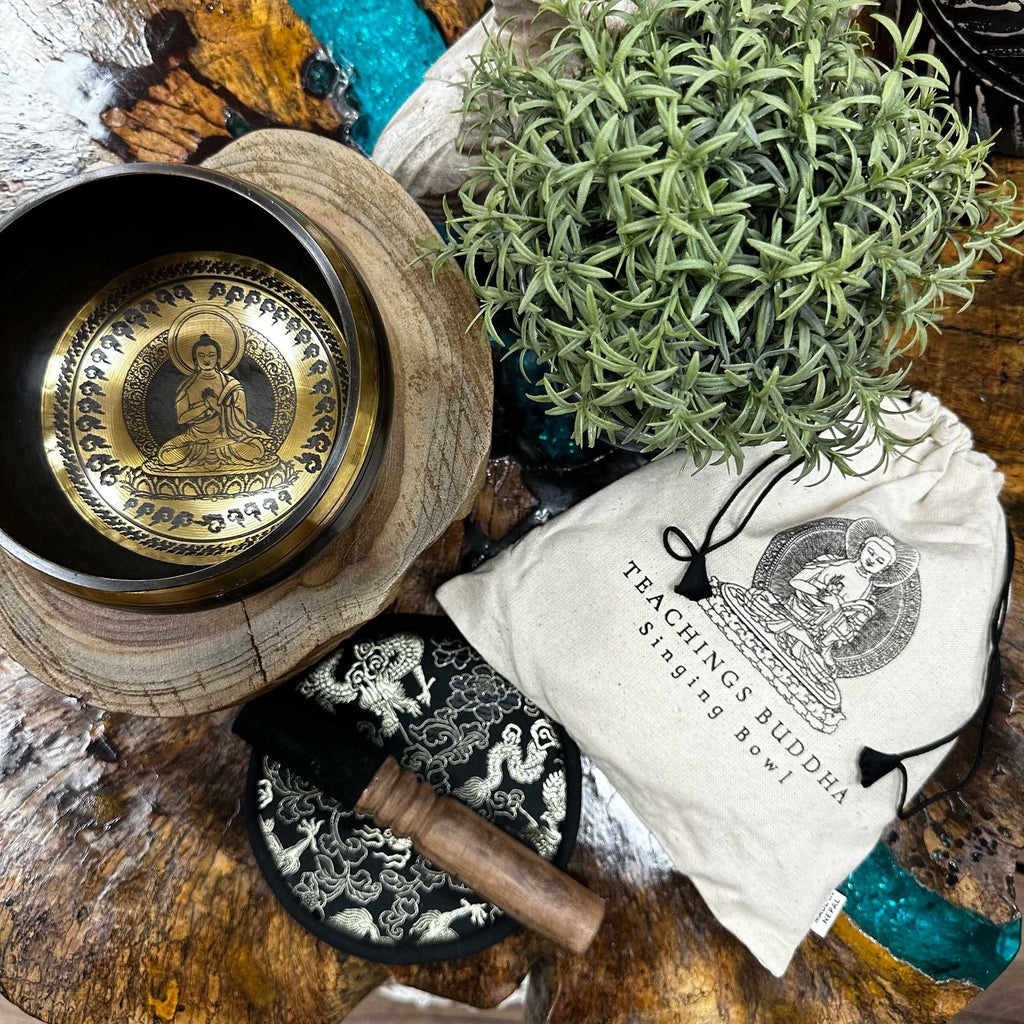 Bol chantant enseignement bouddha posé sur bois avec plante, maillet et pochette, ambiance naturelle pour méditation et harmonisation