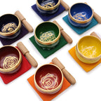 Ensemble de 7 bols chantants chakras posés sur coussins colorés avec maillets, représentant les centres énergétiques du corps