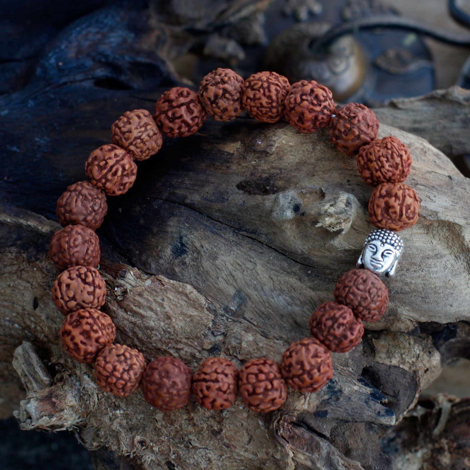 Bracelet en perles rudraksha avec tête de Bouddha marron posé sur bois ambiance méditation