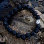 Bracelet en perles rudraksha noir avec tête de Bouddha posé sur bois ambiance méditation