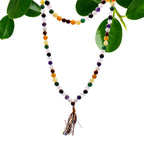 Collier mala 108 perles en pierre naturelle 9 planete astro avec pompon multicouleurs, suspendu avec feuilles vertes en arriere plan, bijou spirituel pour meditation chakra et bien etre