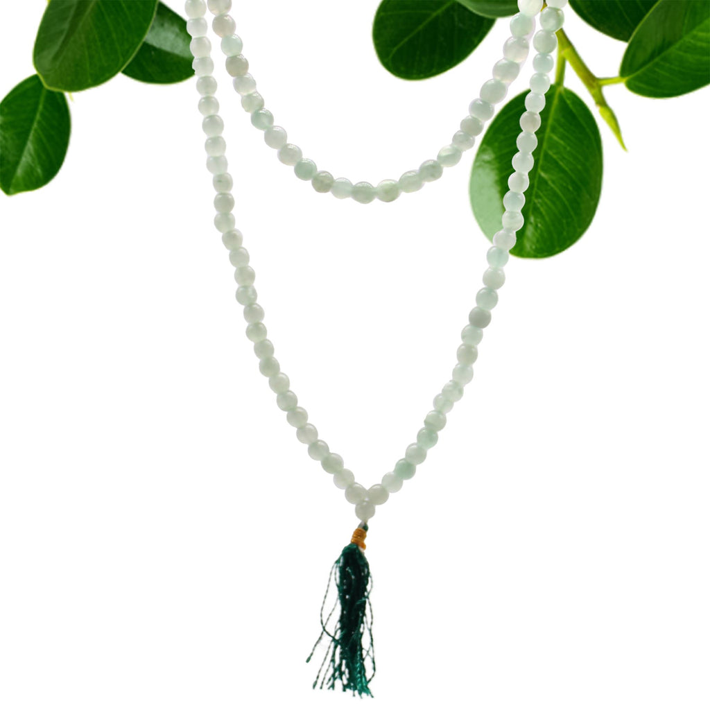 Collier mala 108 perles en pierre naturelle aventurine avec pompon vert, suspendu avec feuilles vertes en arriere plan, bijou spirituel pour meditation chakra et bien etre