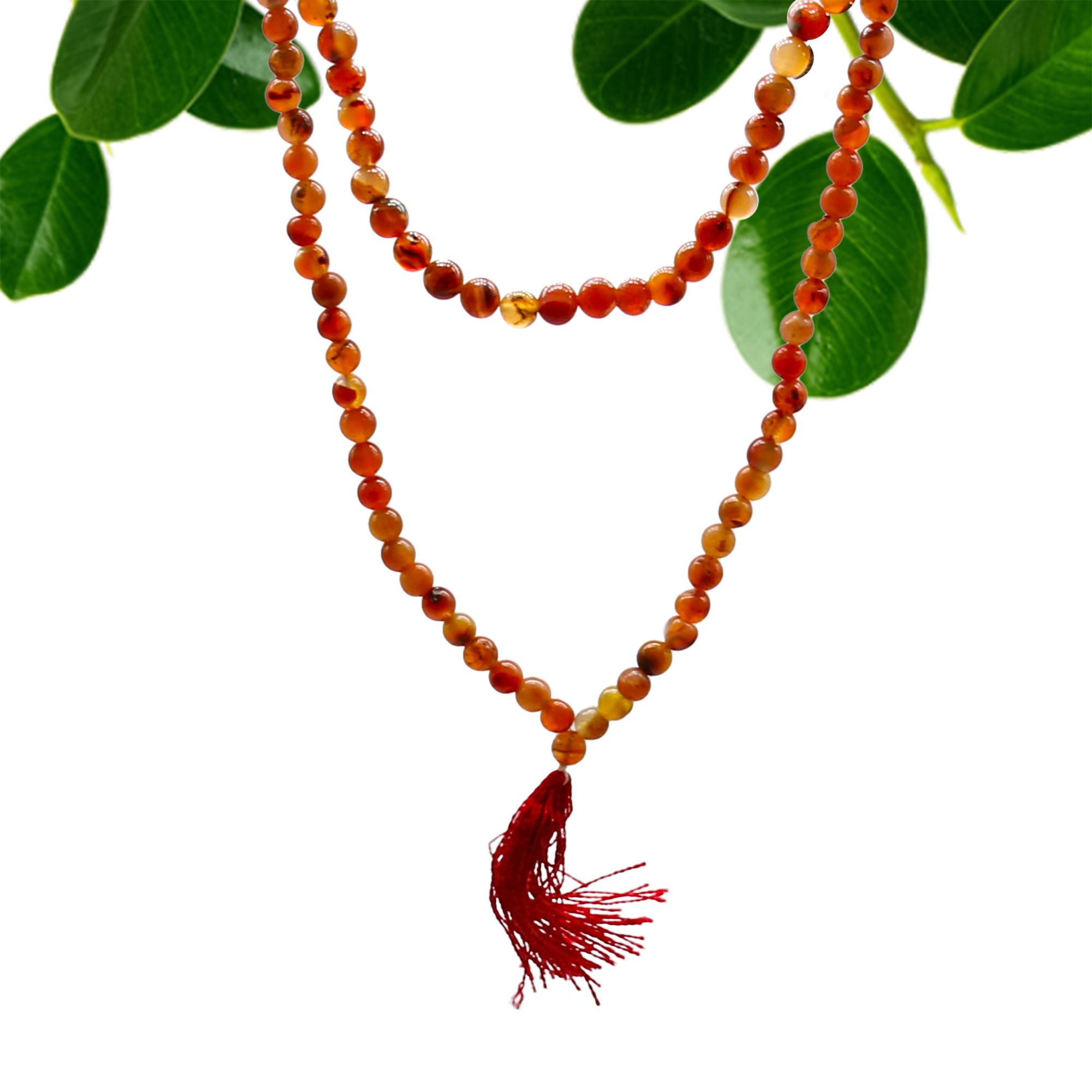 Collier mala 108 perles en pierre naturelle cornaline avec pompon rouge, suspendu avec feuilles vertes en arriere plan, bijou spirituel pour meditation chakra et bien etre