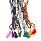 Ensemble de malas 108 perles en pierres naturelles de differentes couleurs avec pompons colores alignes sur fond blanc, incluant amethyste, aventurine, agate noire, oeil de tigre et quartz etc