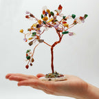 Arbre multicolore tenu dans une main avec pierres naturelles variées, symbole d’équilibre énergétique global
