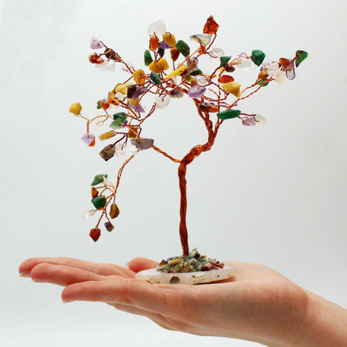 Arbre multicolore tenu dans une main avec pierres naturelles variées, symbole d’équilibre énergétique global