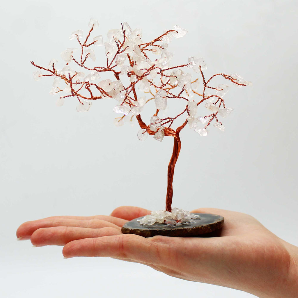 Arbre en cristal de roche avec base en agate noire posé dans une main, branches fines en métal et pierres transparentes