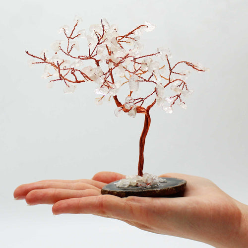 Arbre en cristal de roche avec base en agate noire posé dans une main, branches fines en métal et pierres transparentes