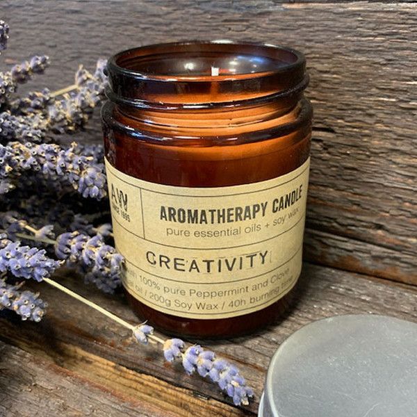 Bougie aromathérapie Créativité à base d’huile essentielle de menthe poivrée et clou de girofle posée sur une surface en bois avec des brins de lavande, ambiance naturelle et relaxante