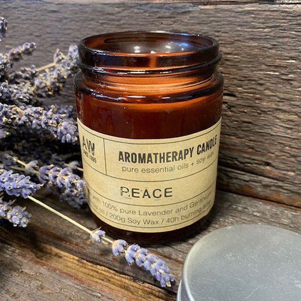 Bougie aromathérapie Peace à base d’huile essentielle de lavande et géranium, posée sur une surface en bois avec des brins de lavande, ambiance naturelle et relaxante