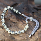 Bracelet en pierre naturelle jaspe dalmatien posé sur bois, symbole de sérénité et énergie spirituelle