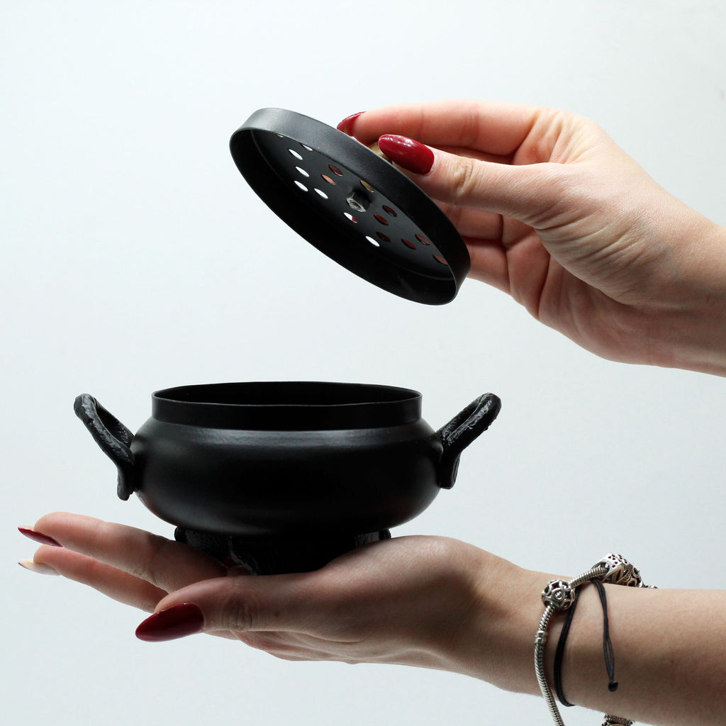 Petit chaudron d’encens en fonte utilisé lors d’un rituel, posé sur main et autre main ouvrant le couvercle