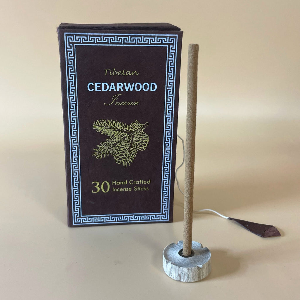 Encens tibétain bois de cèdre avec bâtonnet posé sur support et coffret vert en arrière-plan