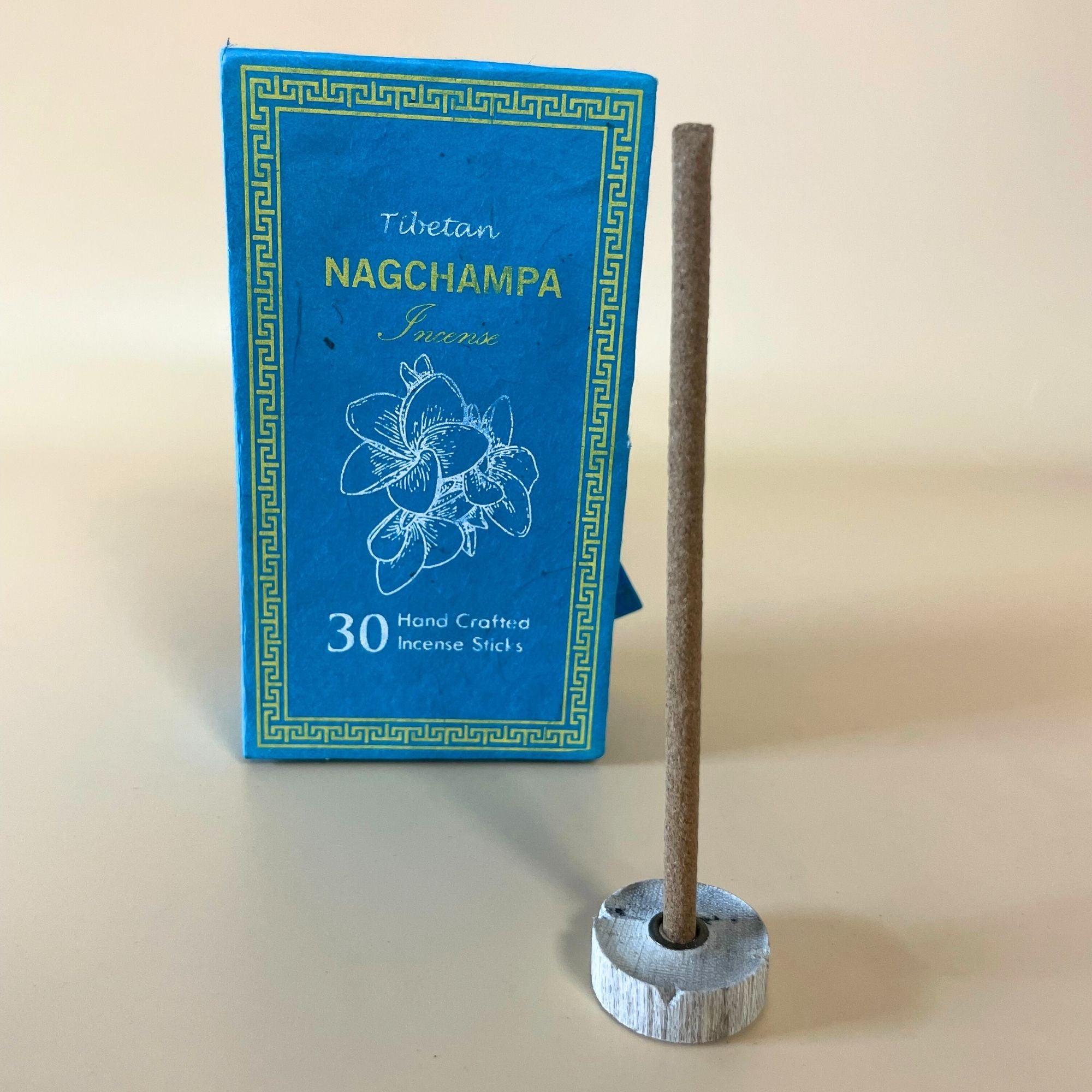 Encens tibétain nag champa avec bâtonnet posé sur support et coffret vert en arrière-plan
