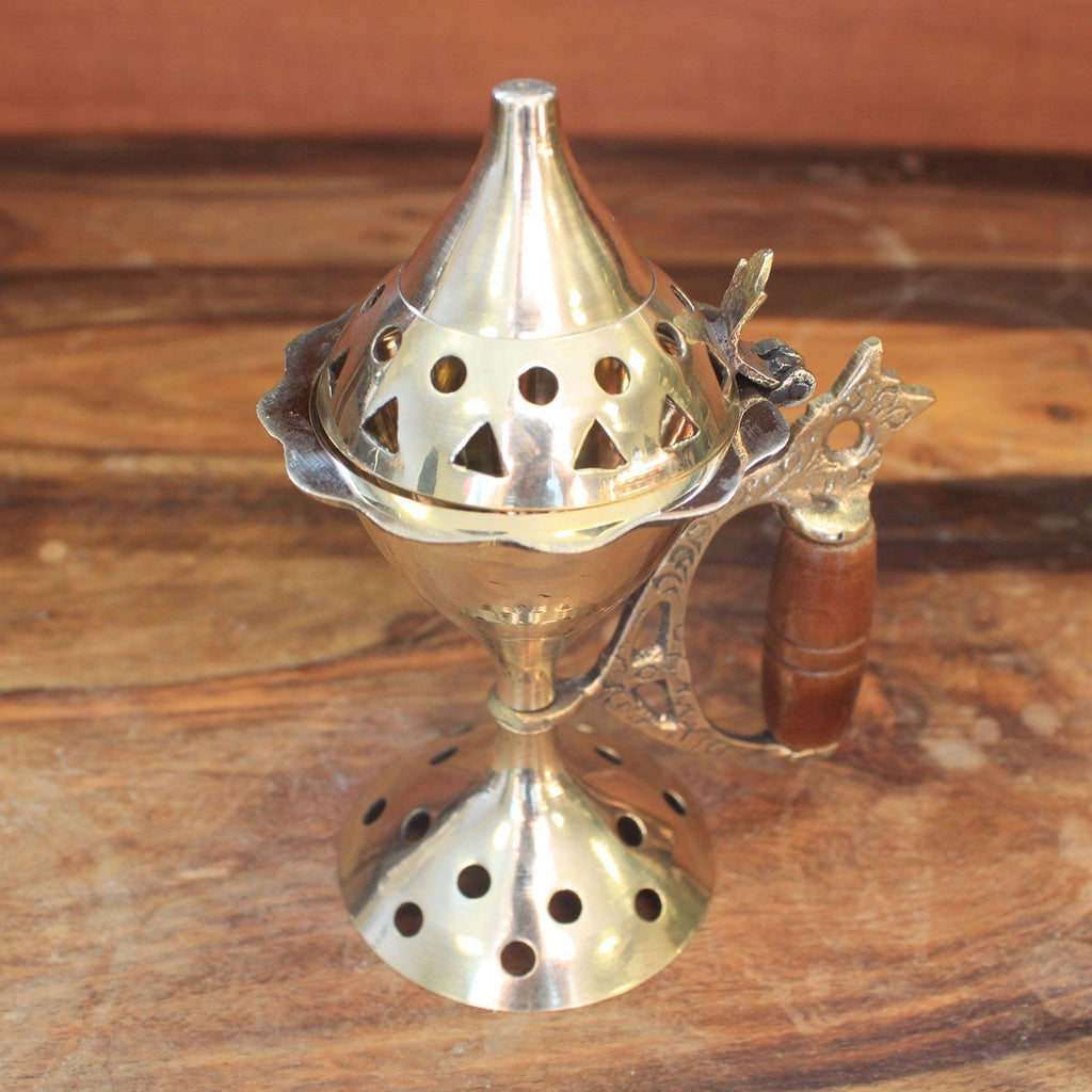 brûleur d’encens en laiton avec manche bois posé sur une table en bois avec encens à côté utilisé pour rituels méditation et parfum d’intérieur