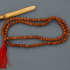 collier mala rudraksha comprenant un mala collier avec perles marron et pompon rouge, sur fond gris