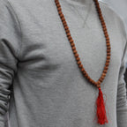 Personne portant un mala rudraksha en collier avec pompon rouge sur un vêtement clair, style minimaliste et naturel.