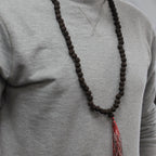 Personne portant un mala rudraksha en collier avec pompon rouge et blanc sur un vêtement clair, style minimaliste et foncé.