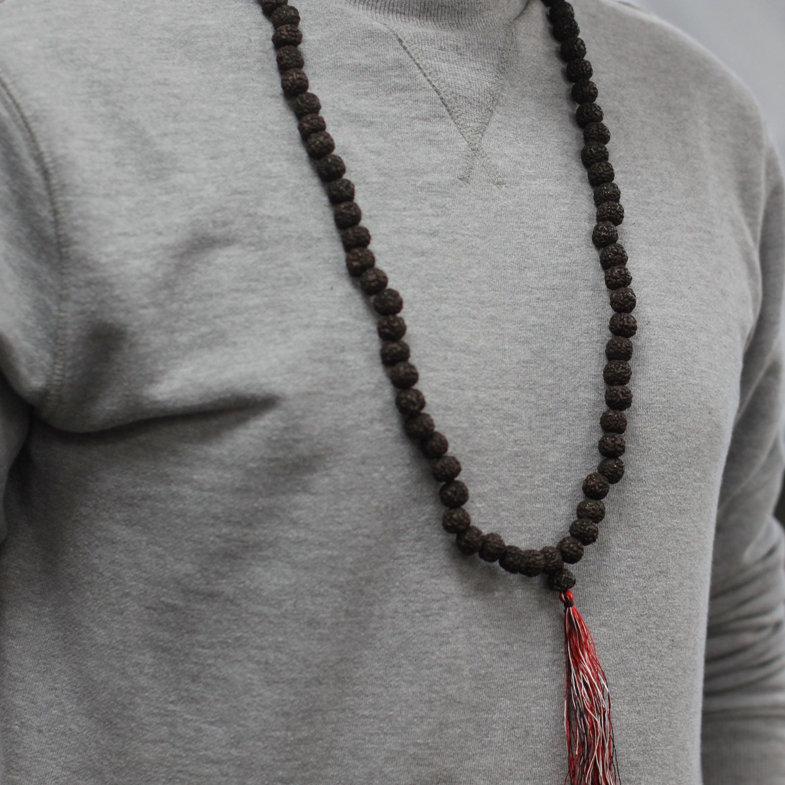 Personne portant un mala rudraksha en collier avec pompon rouge et blanc sur un vêtement clair, style minimaliste et foncé.