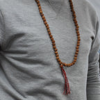 Personne portant un mala rudraksha en collier avec pompon rouge et blanc sur un vêtement clair, style minimaliste et naturel.