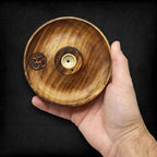 porte encens rond en bois naturel avec symbole om gravé tenu dans la main montrant sa fabrication artisanale et son support pour encens