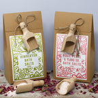 Deux sels de bain 500g Himalaya et rose ylang ylang avec étiquettes vertes et rose et cuillères en bois dans un décor naturel, roses séchées éparpillées sur table en bois